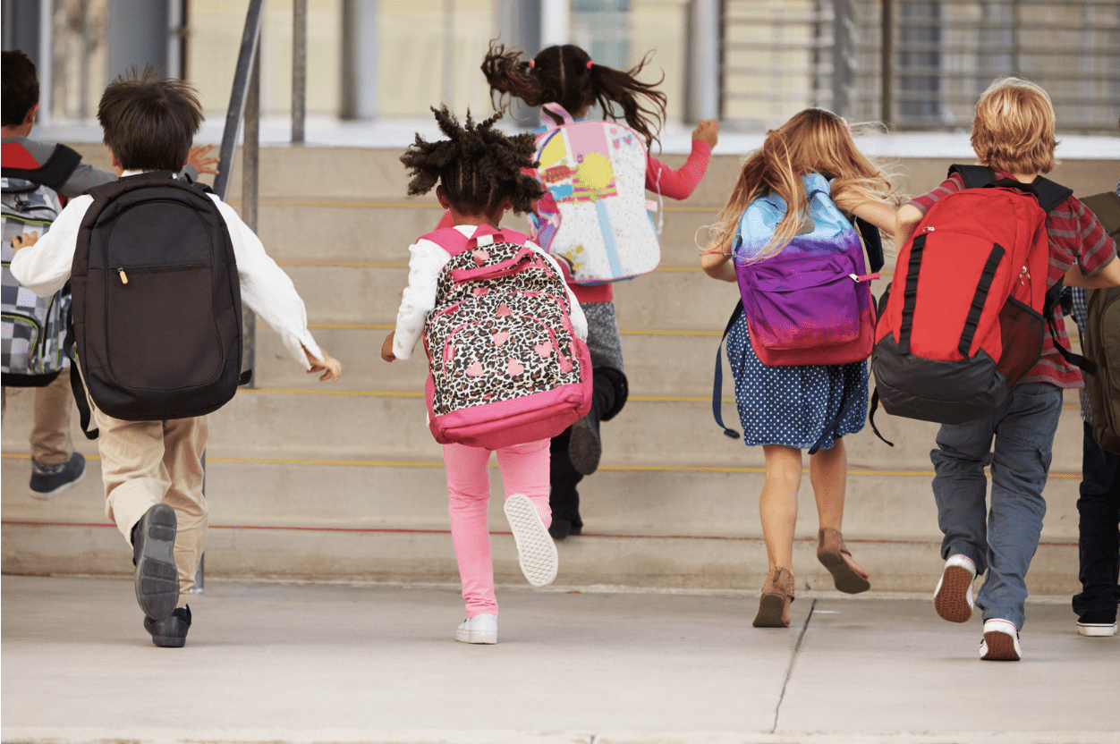 Image of the back of young students running, with backpacks on.