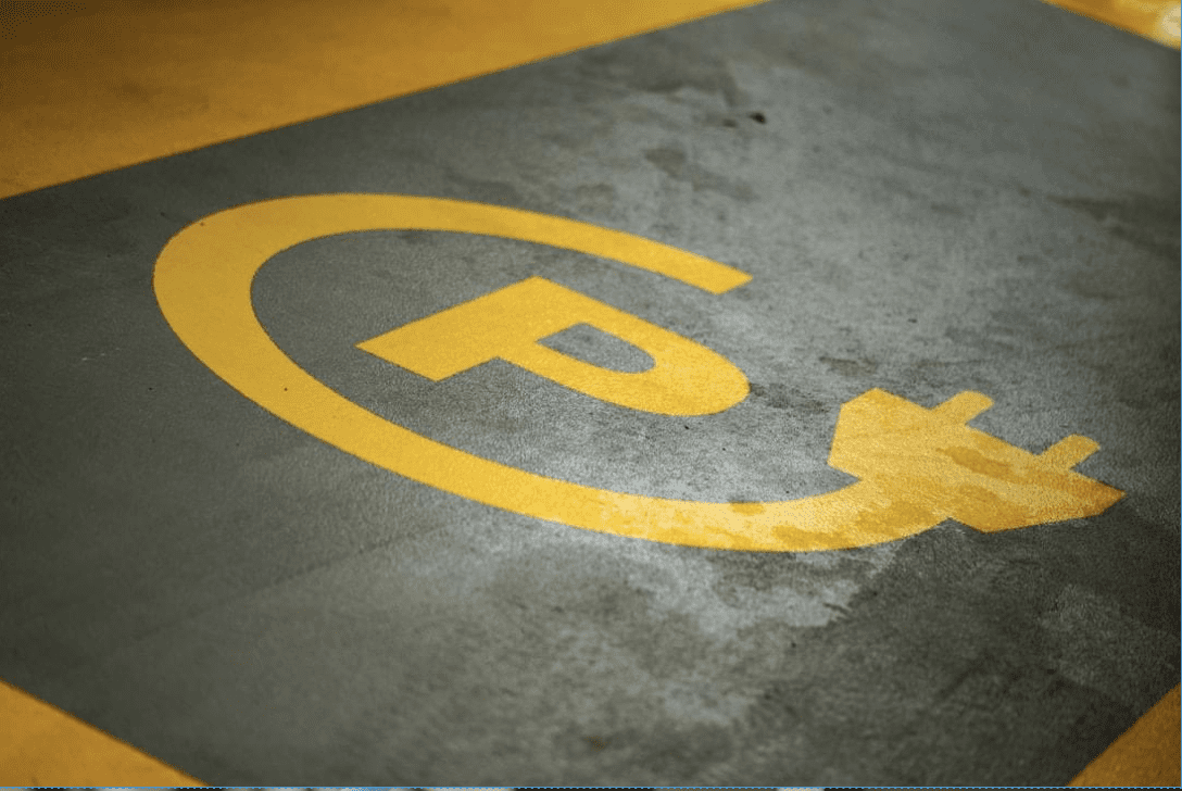 Image of a parking space with an electric cord coming out of it to imply the space is for charging electric vehicles.